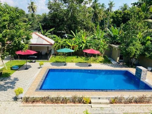 a pool in front of a house with red umbrellas at The Kingslayer Resort in Negombo