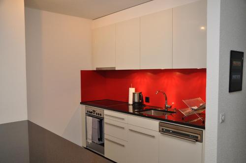 une cuisine avec des placards blancs et un mur rouge dans l'établissement Tulai D74, à Scuol