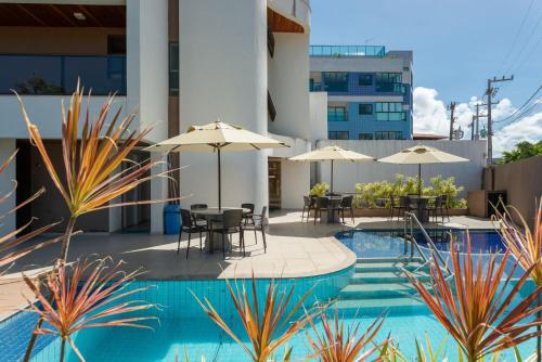 uma piscina com mesas e guarda-sóis num edifício em Praia Central Porto de Galinhas em Porto de Galinhas