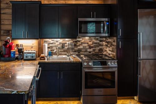 a kitchen with black cabinets and a sink and a stove at stayNantahala - Smoky Mountain Cabins in Aquone