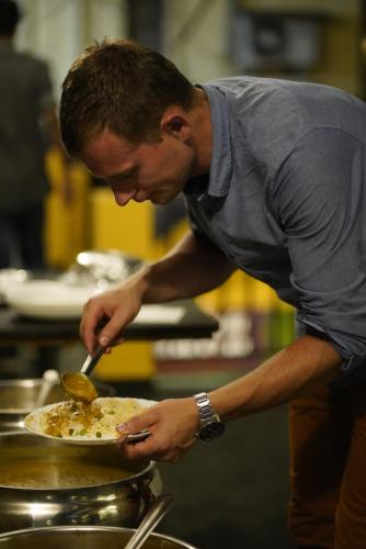 a man preparing a plate of food with a spoon at Fortkochi Beach Inn in Cochin