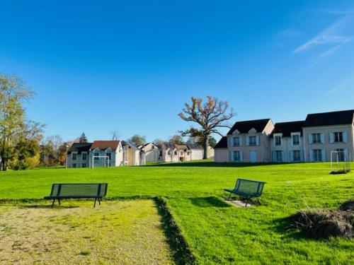 two benches in a grassy field with houses in the background at Appart Hôtel 3* dans une résidence de tourisme in Le Mée-sur-Seine