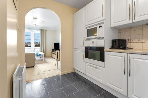 a kitchen with white cabinets and a living room at Modern 1BR flat - free parking + lift in Edinburgh