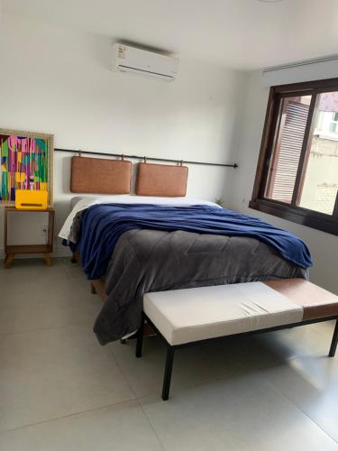 um quarto com uma cama, um banco e uma janela em Apartamento Artístico - Garagem - Ar Condicionado - Excelente Localização em Bento Gonçalves