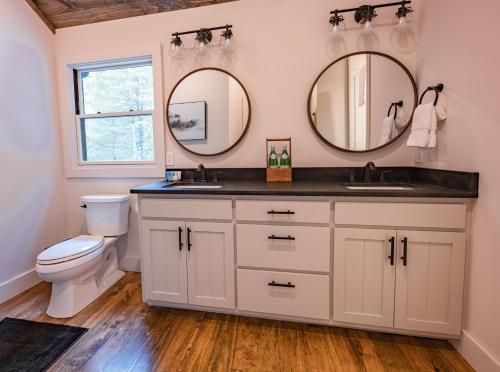 a bathroom with a sink and a toilet and two mirrors at stayNantahala - Smoky Mountain Cabins in Aquone