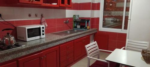 eine rote Küche mit Mikrowelle und Spüle in der Unterkunft Villa Saraya in Mehdiya-Plage