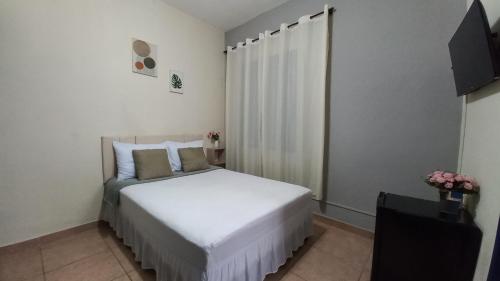 um quarto com uma cama branca e uma televisão em Suíte em Hospedaria no Centro Histórico em Ouro Preto