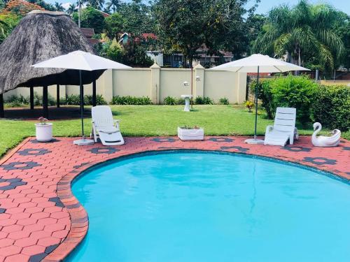 a swimming pool with two lawn chairs and umbrellas at Q’s in Empangeni