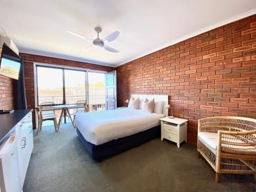 een slaapkamer met een bed en een bakstenen muur bij Pelican Motor Inn in Merimbula