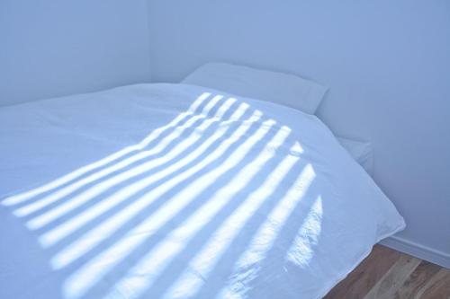 a white bed with a ray of sunlight on it at CASA Kamakura Espresso&BED in Kamakura