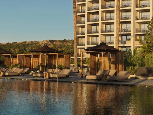 a pool with chairs and umbrellas next to a building at Ammades All Suites Beach Hotel & Spa - Adults Only in Faliraki