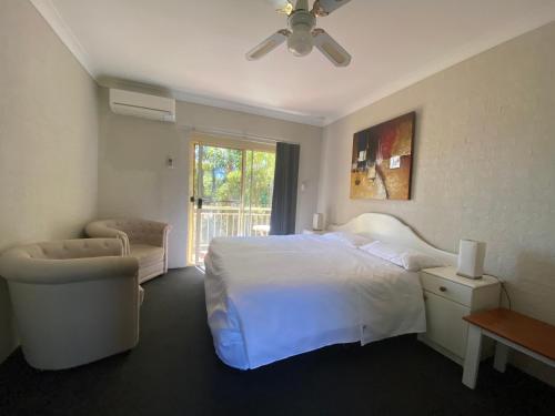 a bedroom with a bed and a chair and a window at Mollymook Paradise Haven Motel in Mollymook