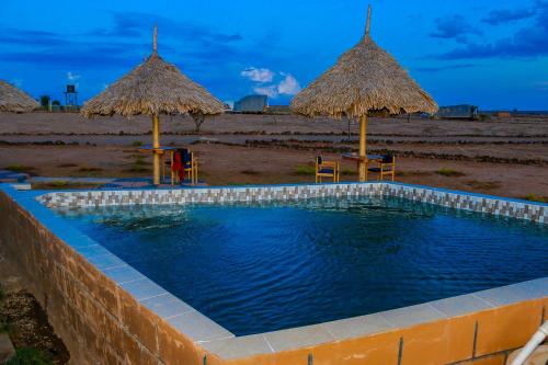 einen Pool mit zwei Strohschirmen und einem Strand in der Unterkunft Amanya King Lion 1-Bed Wigwam in Amboseli in Amboseli-Nationalpark