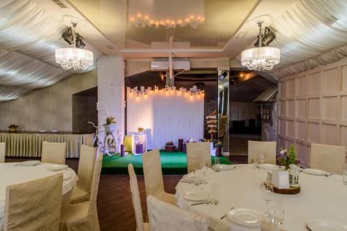 uma sala de jantar com mesas e cadeiras brancas e lustres em Knyazhyi Dvir em Sokilʼnyky