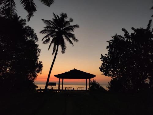 a gazebo with a palm tree and the ocean at sunset at Munroe Coconut Homestay in Munroe Island