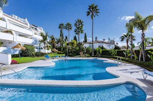 a swimming pool in front of a building with palm trees at Molo Bahia Apartment Near the beach in Marbella