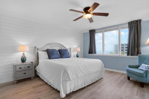 a bedroom with a bed with a ceiling fan and a blue chair at Heron 507- A Wave From It All in Fort Walton Beach