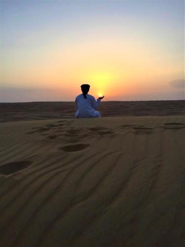 a person sitting in the desert watching the sunset at Desert Moments Glamping - full privacy in Muntarib