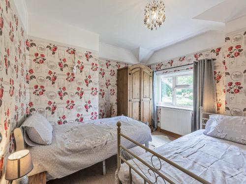 a bedroom with two beds and floral wallpaper at Flyby Cottage in Symonds Yat