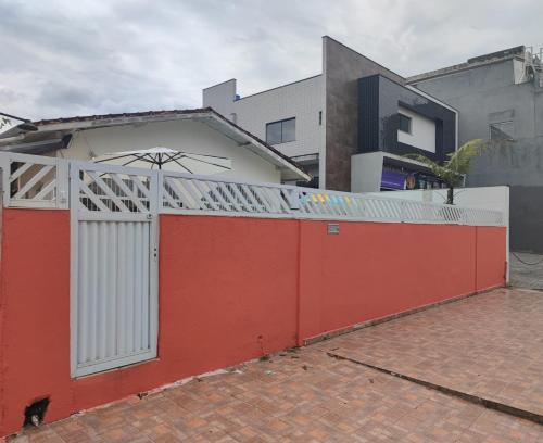 einem roten Zaun mit einem weißen Tor vor einem Gebäude in der Unterkunft Jdu Hostel e Bar in Bertioga