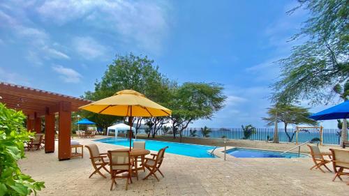 um pátio com cadeiras, um guarda-sol e uma piscina em Hostería del Parque em Machalilla