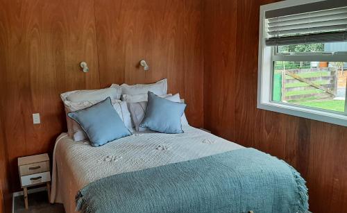a bedroom with a bed with blue pillows and a window at Waiora cottage in Otaki