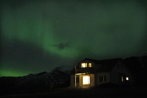 ein Haus unter den grünen Nordlichtern in der Nacht in der Unterkunft Sauðanes Guesthouse in Höfn
