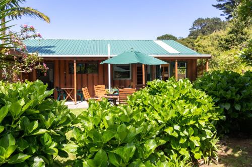 a house with a green roof with chairs and an umbrella at Aotea Lodge Great Barrier in Tryphena