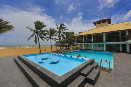 a swimming pool next to a building with a beach at Catamaran Beach Hotel in Negombo