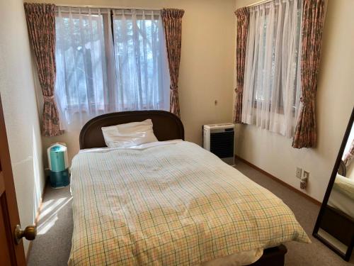 a bedroom with a bed with a checkered blanket and windows at Cottage 62 Seseraginomori Kyu-karuizawa in Karuizawa