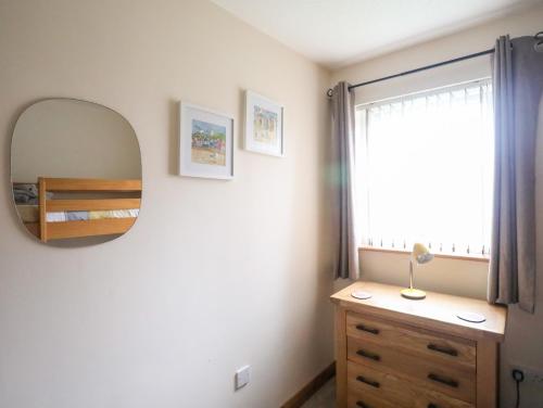 a bedroom with a mirror and a dresser and a window at Sandy Toes in Rhosneigr