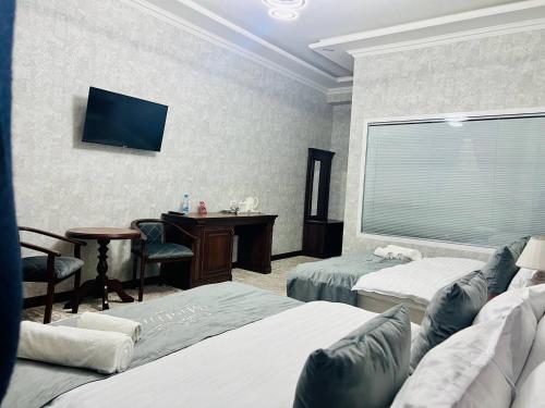 a room with two beds and a desk and a television at Medina Hotel Samarkand in Samarkand
