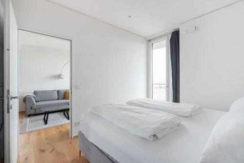 a white bedroom with a bed and a chair at Hoch hinaus, neu und stilvoll mit Pool am Dach in Vienna