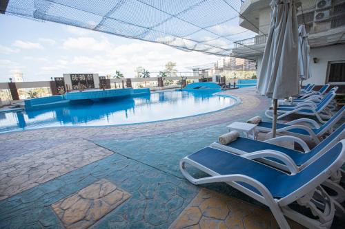 AIFU Hotel El Montazah Alexandria في الإسكندرية: مسبح مع كراسي صالة ومظلة
