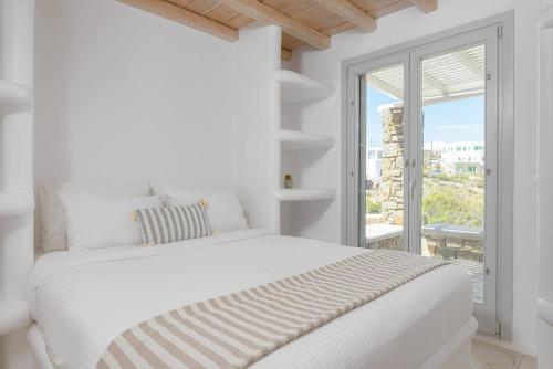 a white bedroom with a white bed and a window at Koumi Homes Mykonos in Elia