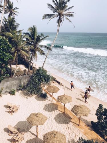 a beach with some straw umbrellas and the ocean at Morena Boutique Hotel Weligama in Midigama