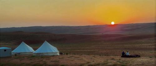 two tents in the desert with the sunset in the background at Desert Moments Glamping - full privacy in Muntarib