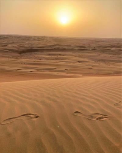 a sunset over the ocean with footprints in the sand at Desert Moments Glamping - full privacy in Muntarib