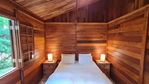 a bed in a wooden room with two lamps at Chalé Arado 313 in Monte Verde