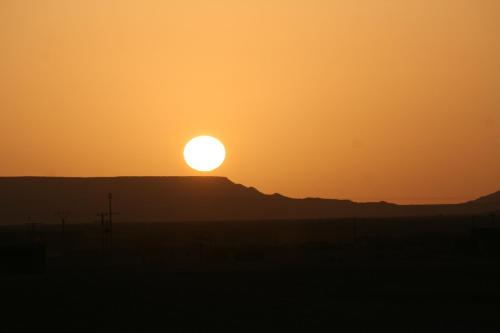 a sunset in the desert with the sun setting on a hill at Casbah d'hôte La Jeanne Tourisme Ecologique in Boumalne