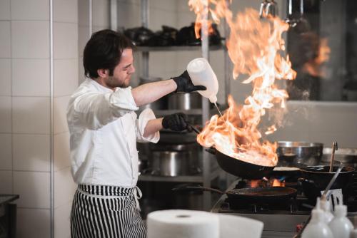 a man cooking food in a pan in a kitchen at Hotel Borovi Forest Resort & Spa in Sjenica