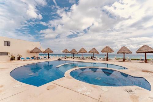 a swimming pool with umbrellas and the ocean at Cancun Hotel Zone, Beachfront 2 BR Apartment - Prime Location in Cancún
