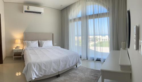 Beach front Le Bon villa في مسقط: غرفة نوم بسرير ابيض ونافذة كبيرة
