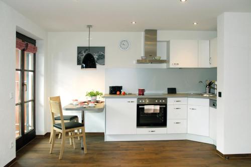 オーベルストドルフにあるGästehaus Rappenkopfの白いキャビネット、テーブルと椅子付きのキッチンが備わります。