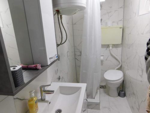 a white bathroom with a toilet and a sink at Apartman Bagdala in Kruševac