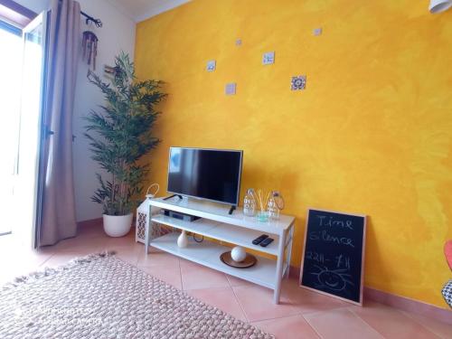 a living room with a tv on a yellow wall at Beach House Haller in Aljezur