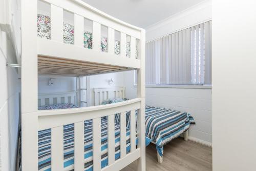 Ce lit superposé blanc se trouve dans un dortoir doté d'un lit bébé. dans l'établissement Forster Holiday Lodge 18, à Forster