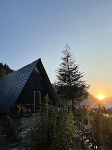 a barn with the sun setting in the background at Himalayan Manor A-Frame House in Sainj