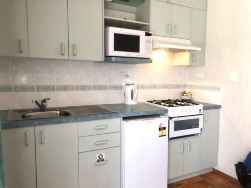 a kitchen with white cabinets and a sink and a microwave at Alexandra Parklife Studio 3 in Alexandra