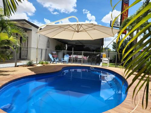 una piscina con sombrilla junto a una casa en Charters Towers Motel, en Charters Towers